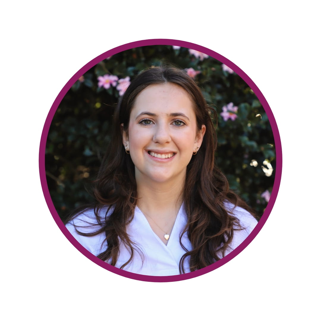 Picture of smiling dark-haired woman standing in front of a tree background. The picture is bordered by a purple circle. 